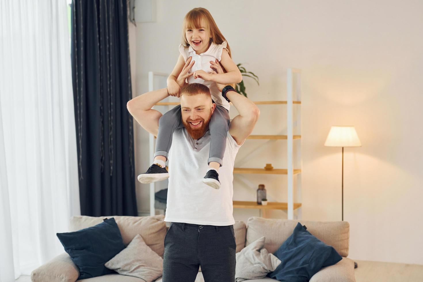 ragazza seduta su il le spalle. padre con il suo poco figlia è a casa insieme foto