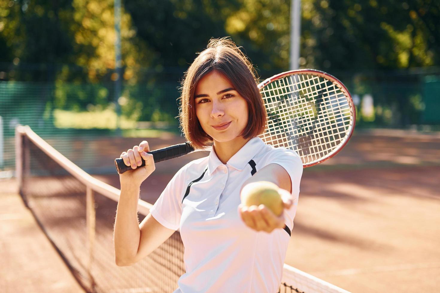 in piedi con racchetta nel mano. femmina tennis giocatore è su il Tribunale a giorno foto