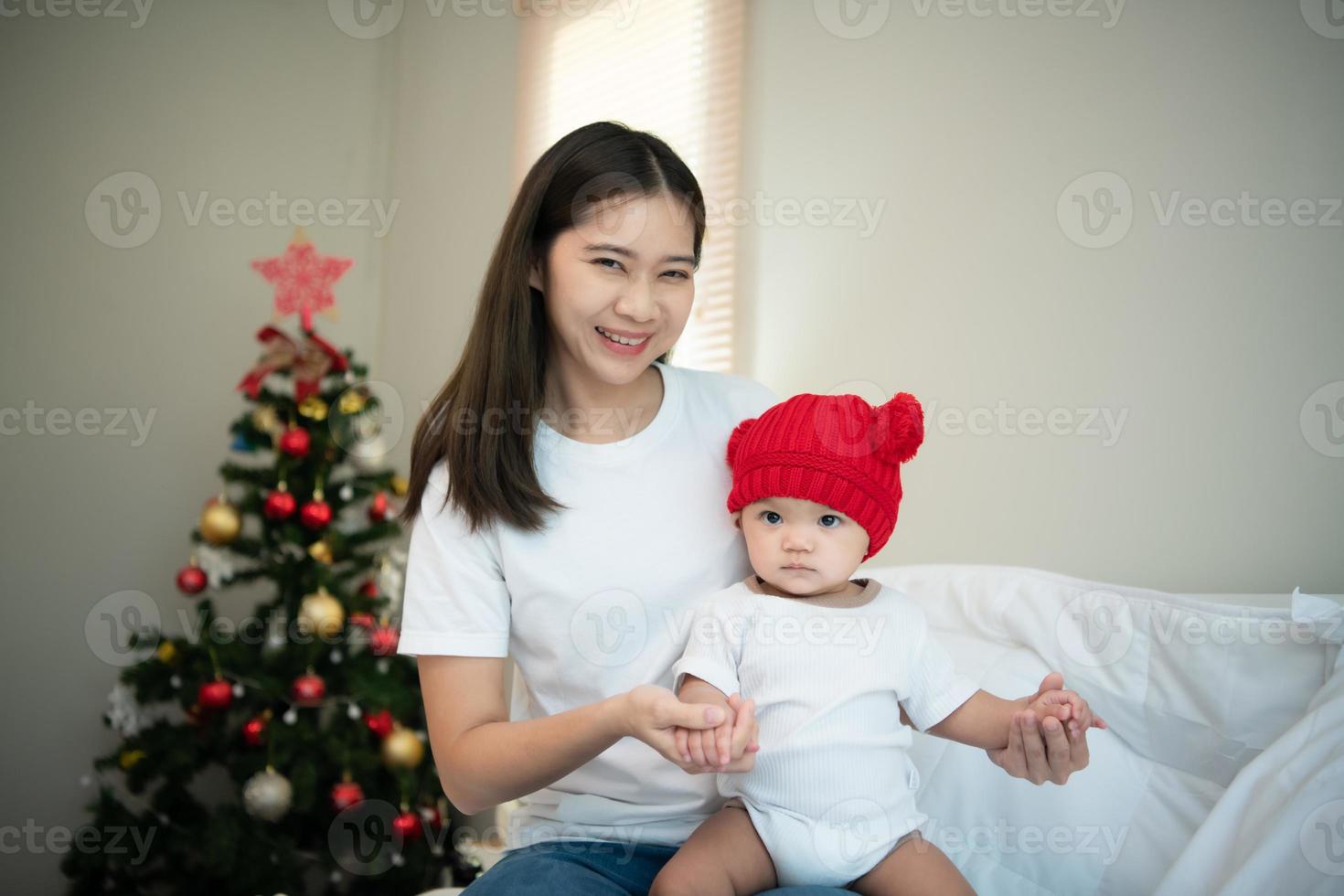 madre e neonato bambino indossare rosso cappelli nel il bianca Camera da letto, caldo luce del sole nel il sera di il giorno foto