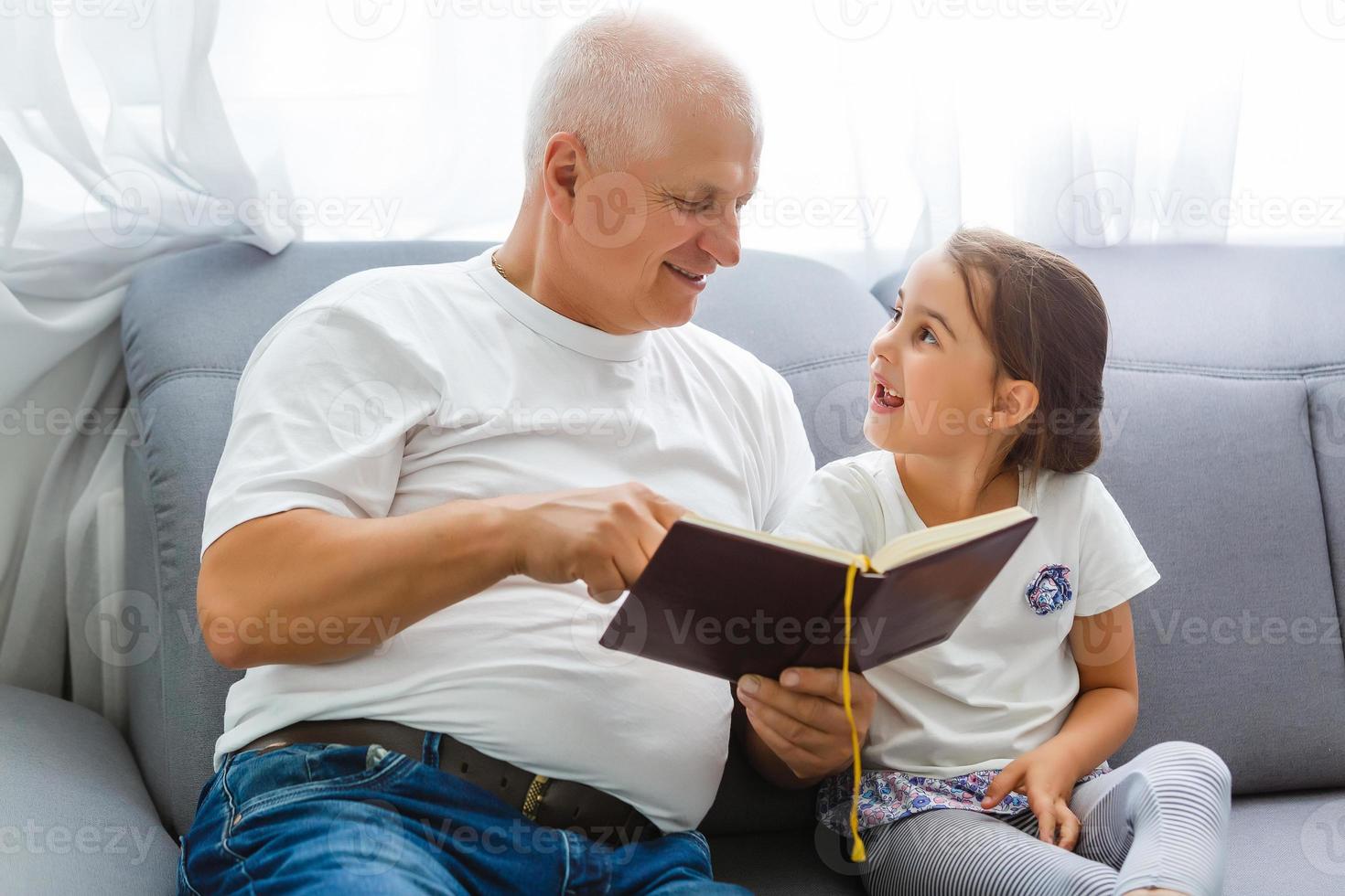 contento poco ragazza con nonno lettura storia libro a casa foto