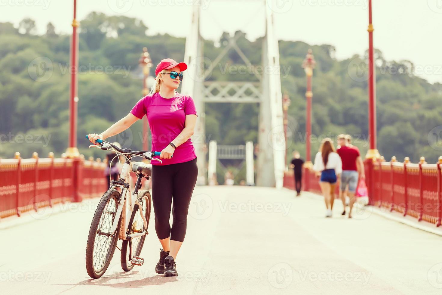 indietro Visualizza di giovane sottile donna in piedi a bicicletta su pietroso marciapiede sotto chiaro blu cielo sfondo. attivo stile di vita e vacanze concetto. foto