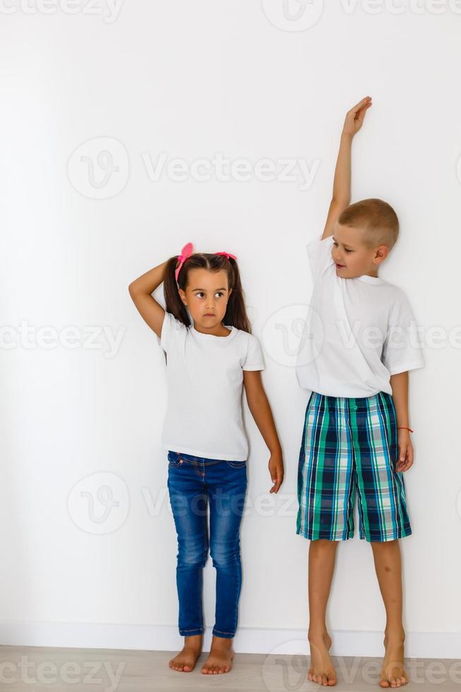 poco ragazzo e ragazza misurazione loro altezza isolato su bianca sfondo foto