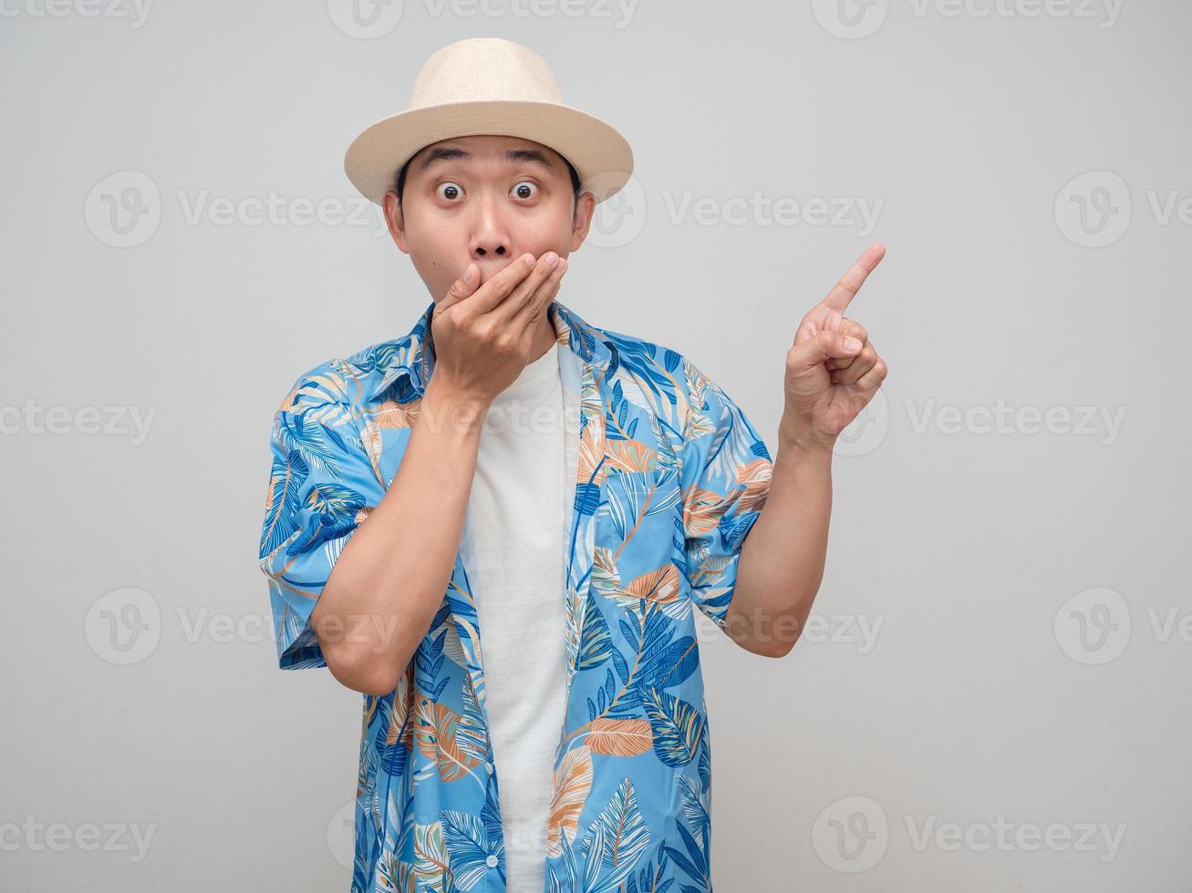 giovane uomo indossare cappello spiaggia camicia si sente scioccato vicino il suo bocca gesto punto dito foto