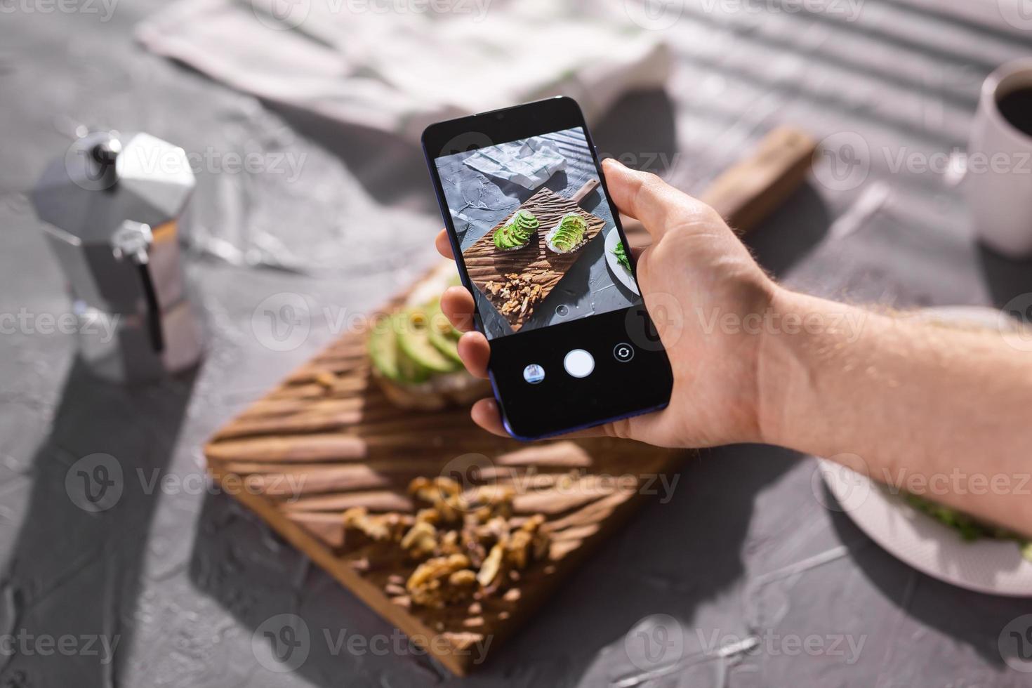 mani prendere immagini su smartphone di Due bellissimo salutare acida crema e avocado panini dire bugie su tavola su il tavolo. sociale media e cibo concetto foto