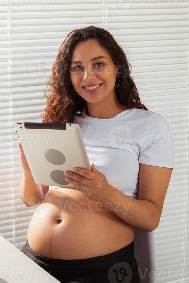 incinta donna utilizzando digitale tavoletta. prima colazione volta. tecnologia e gravidanza concetto. foto