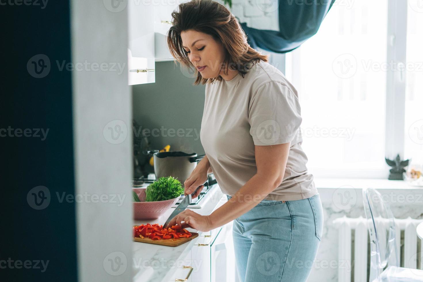 bellissimo brunetta giovane donna più dimensione corpo positivo cucinando insalata nel cucina a il casa foto