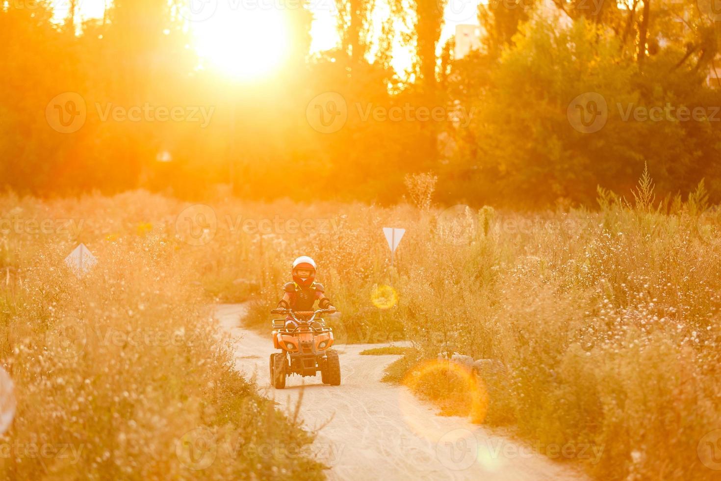 contento poco ragazza giocando su strada a il giorno volta. lui guida su quadrilatero bicicletta nel il parco. bambino avendo divertimento su il natura. concetto di felicità. foto
