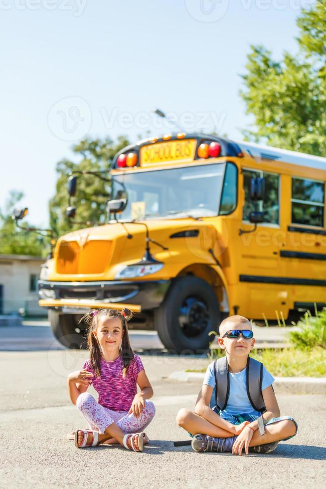 ridendo sorridente caucasico ragazzo alunno ragazzo con divertente viso espressione a piedi vicino giallo autobus su 1 settembre giorno. formazione scolastica e indietro per scuola concetto. bambino allievo pronto per imparare e studia. foto