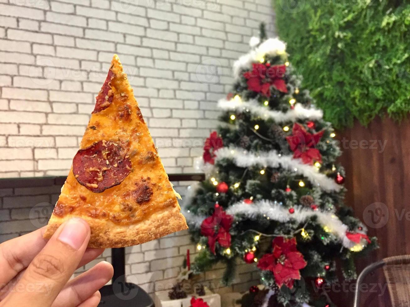 mano tenuto Pizza fetta con Natale albero decorazione sfondo. foto