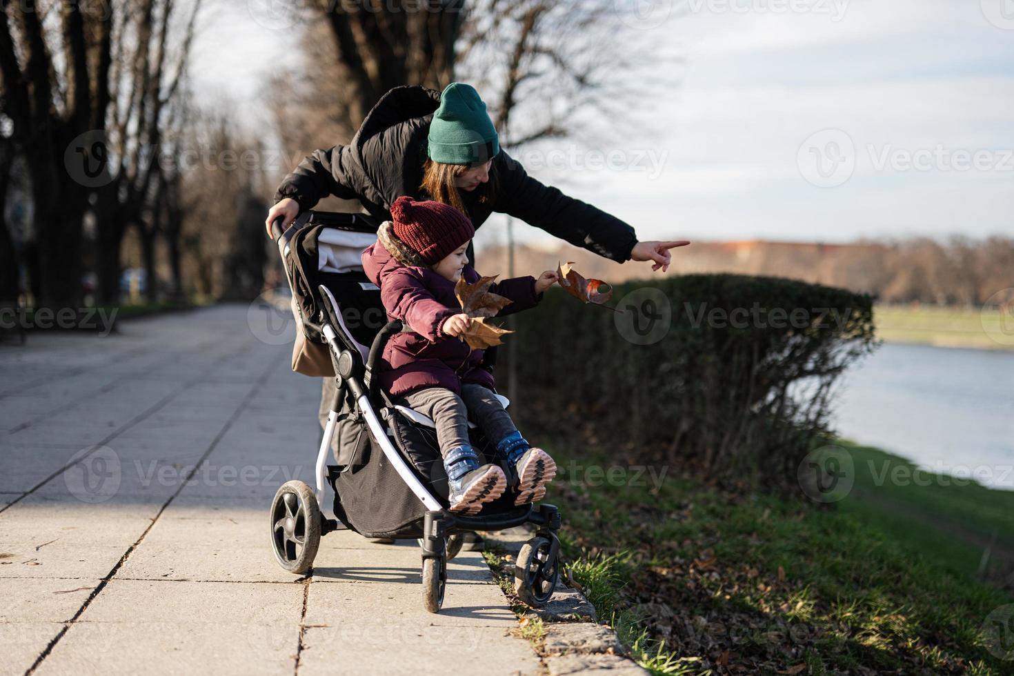 giovane donna nel città parco con bambino passeggino. caldo autunno tempo metereologico per all'aperto attività. foto