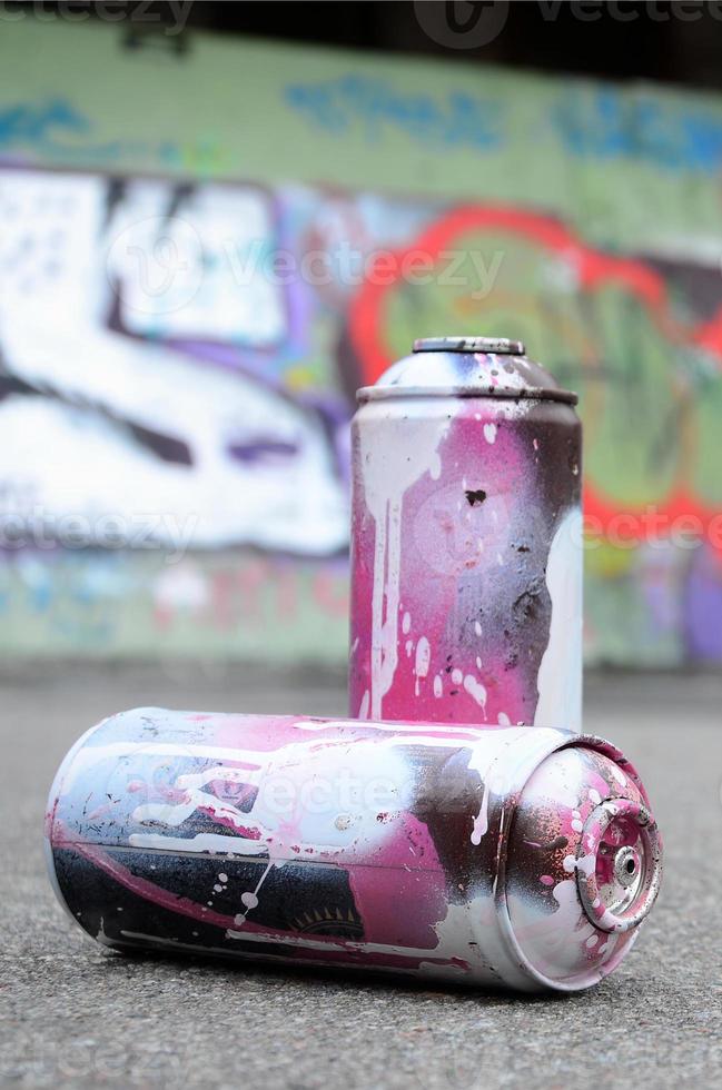 un' pochi Usato spray lattine con rosa e bianca dipingere menzogna su il asfalto contro il sfondo di un' dipinto parete nel colorato graffiti disegni foto