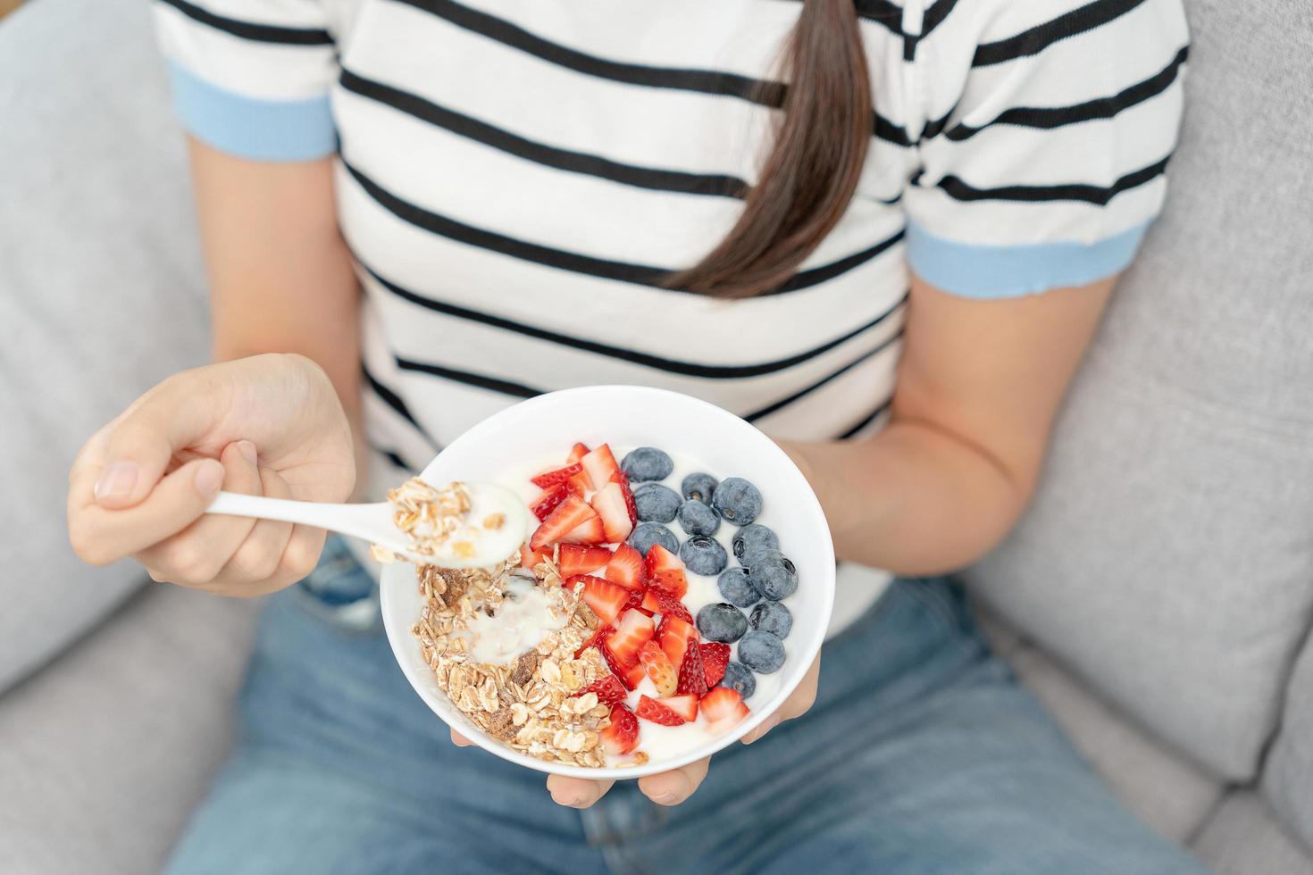 donna avendo delizioso salutare prima colazione a casa su mattina. Salute cura femmina mangia Yogurt con muesli e bacca frutta. salutare cibo, vitamine, pulito dieta, dieta, disintossicazione, vegetariano, biologico cibo. foto