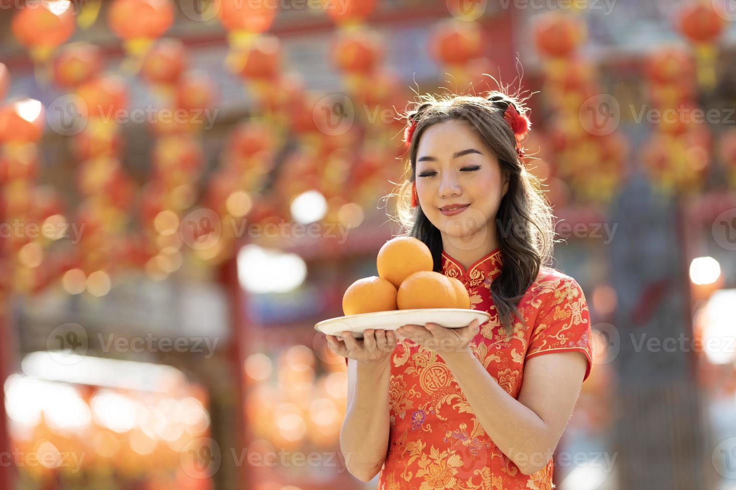 asiatico donna nel rosso cheongsam qipao vestito è offerta mandarino per il ancestrale Dio dentro Cinese buddista tempio durante lunare nuovo anno per migliore desiderio benedizione e bene fortuna concetto foto