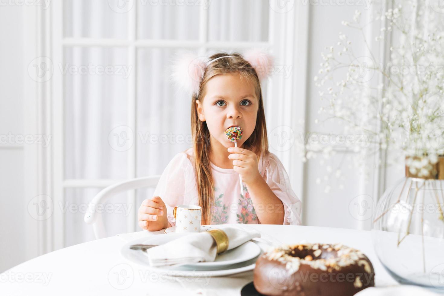 divertente carino poco ragazza con lungo capelli nel leggero rosa vestito Tenere popcake nel mani su festivo tavolo nel luminosa vivente camera a casa. Natale volta, compleanno ragazza foto