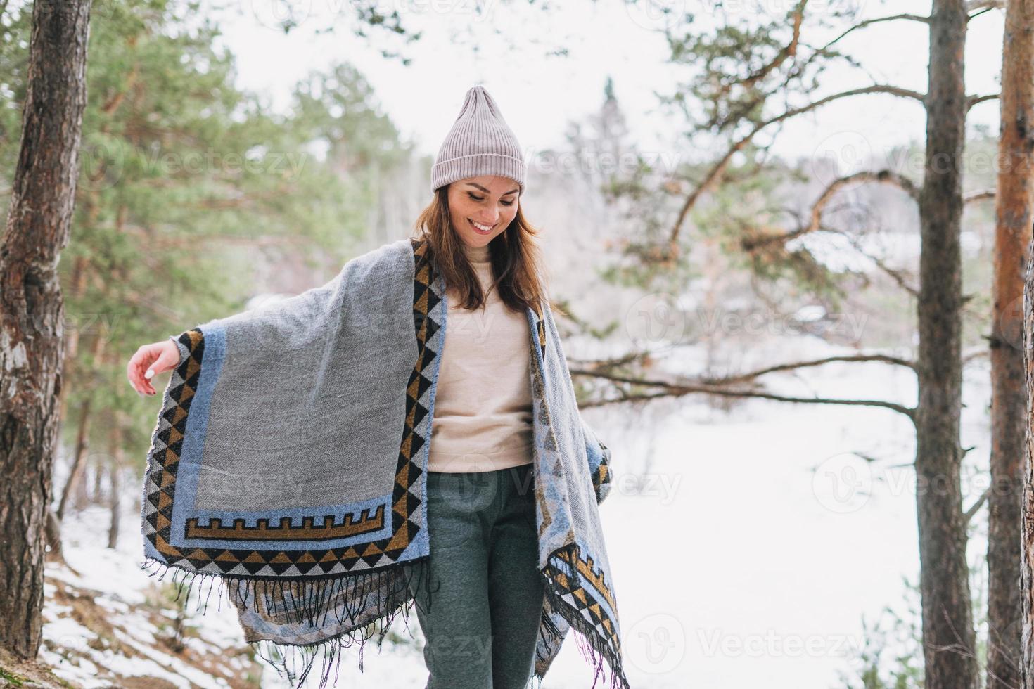 giovane brunetta bellissimo donna nel cappello e grigio poncho nel il inverno foresta foto