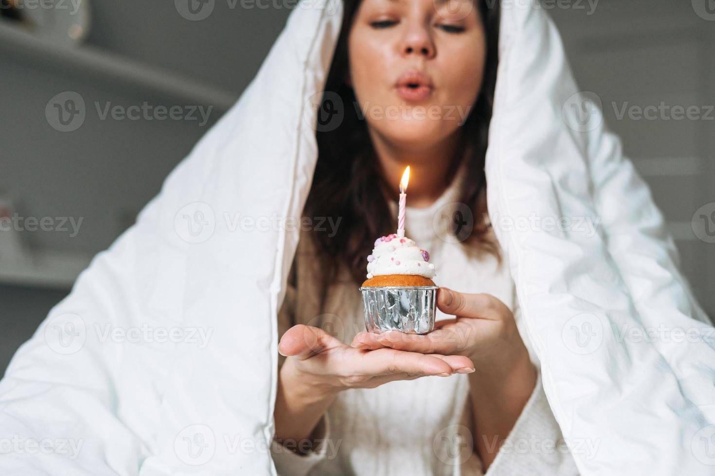 giovane adulto contento bellissimo donna quaranta anni più dimensione corpo positivo nel bianca coperta con festivo Cupcake con candela nel mani su letto a casa festa, compleanno ragazza foto