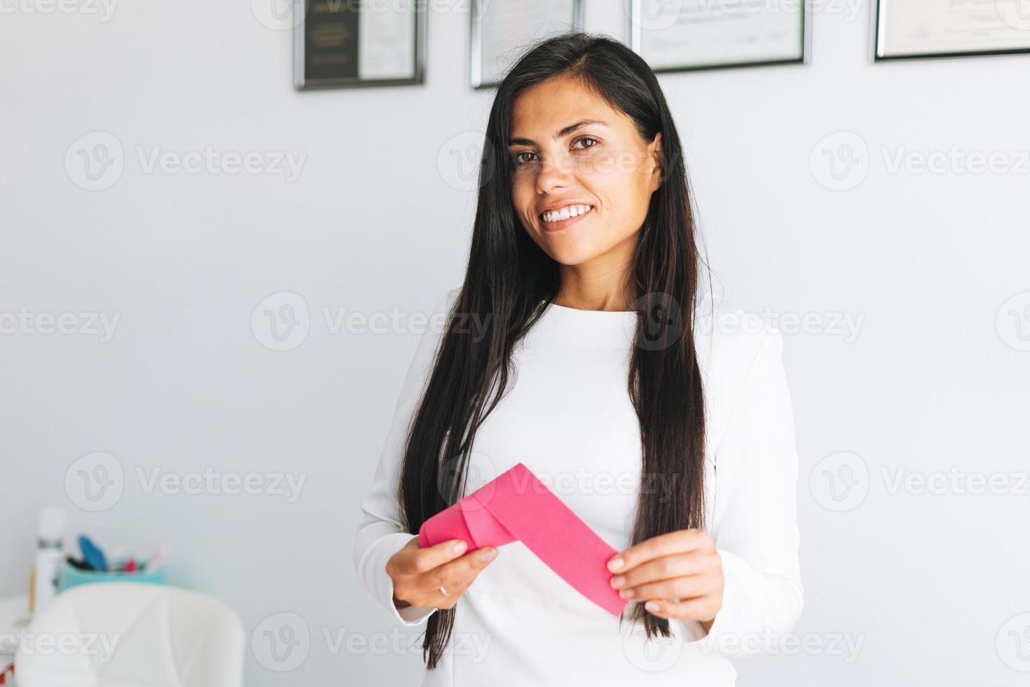 giovane bellissimo brunetta donna con lungo capelli cosmetologo Tenere nastro nastro nel mani nel ufficio. giovane medico con kinesio nastro foto