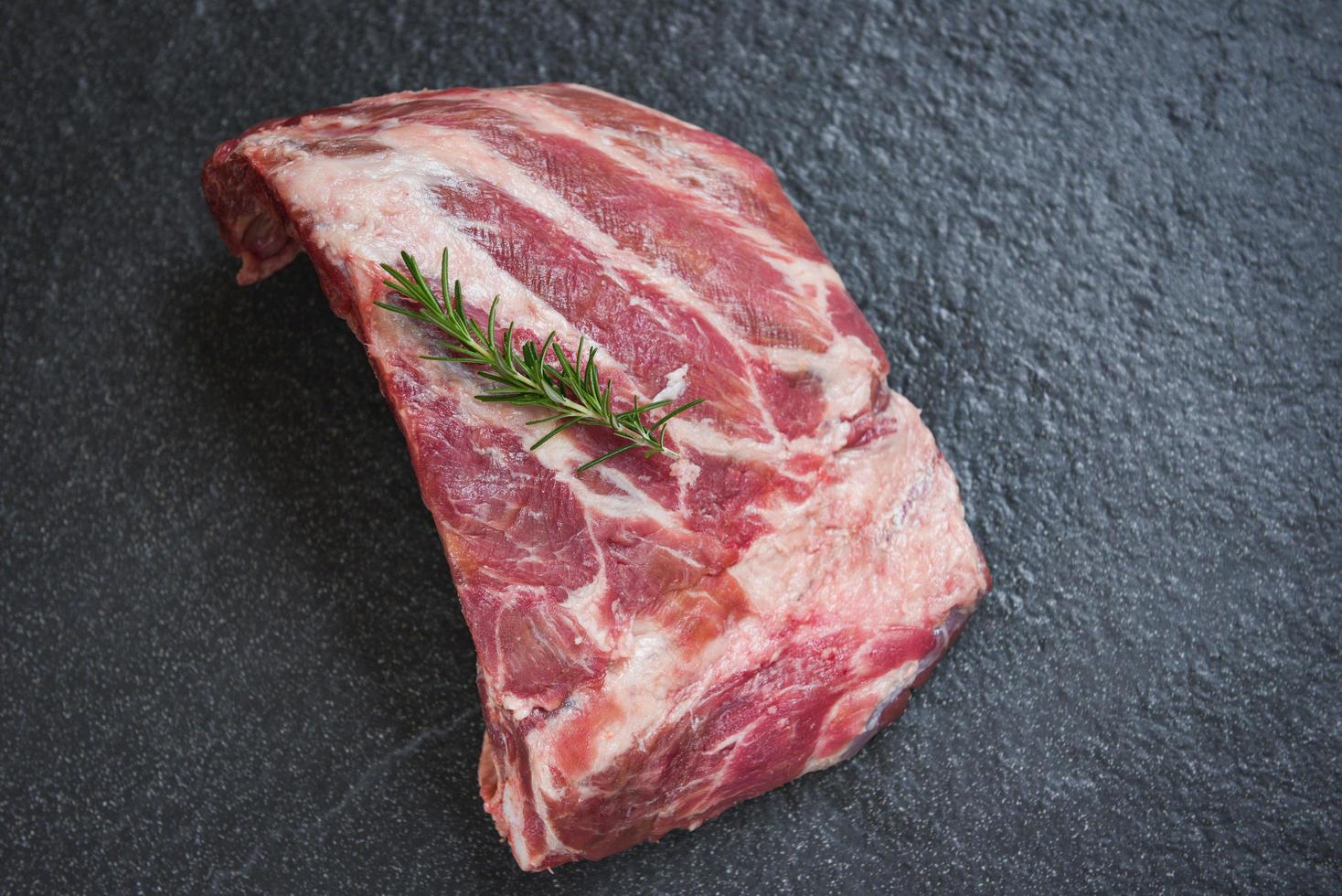 costolette di maiale crude carne su sfondo nero piatto - costolette di maiale fresche per cucinare arrosto o alla griglia, osso di maiale con rosmarino foto
