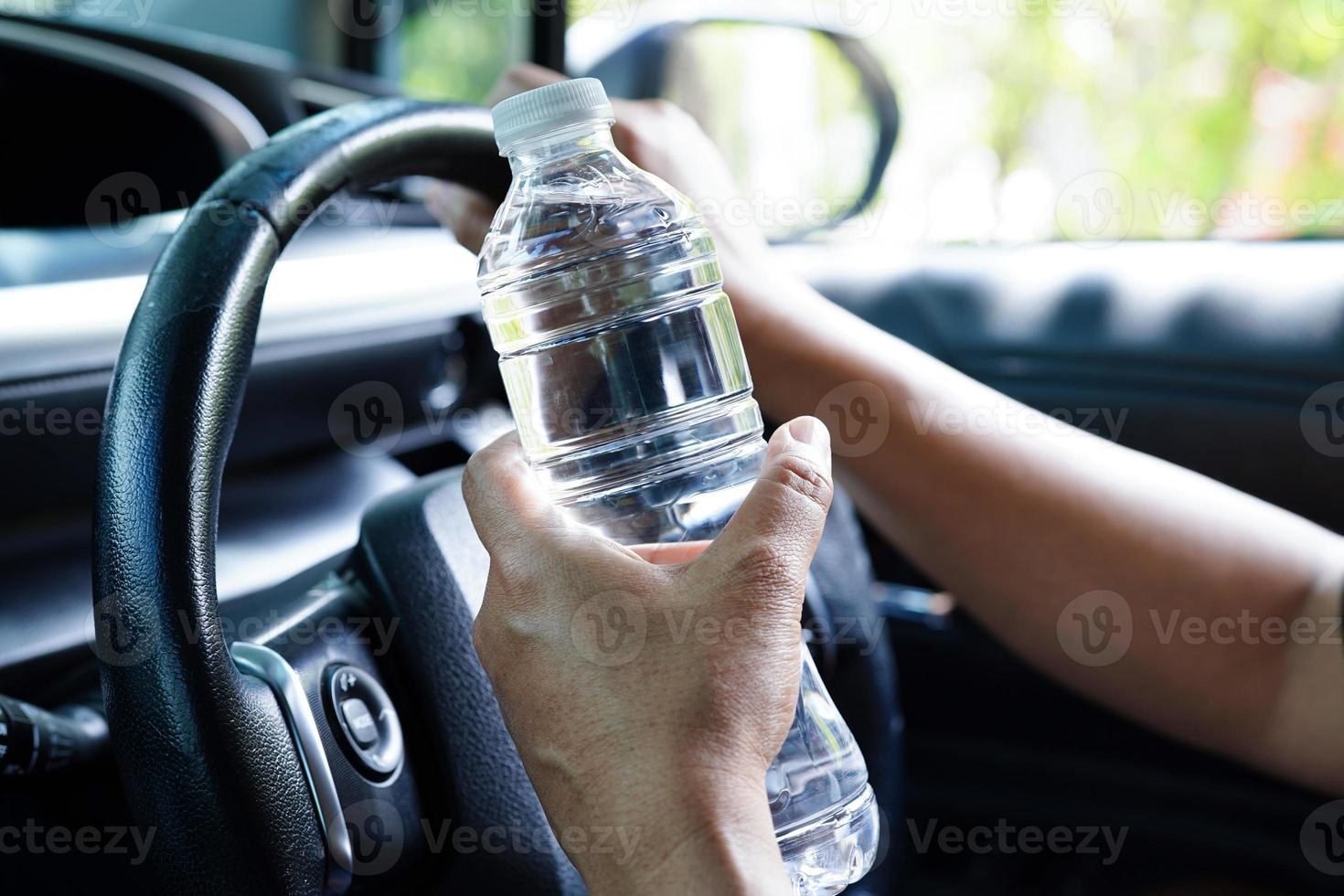 asiatico donna autista hold freddo acqua per bevanda nel macchina, pericoloso e rischio un incidente. foto