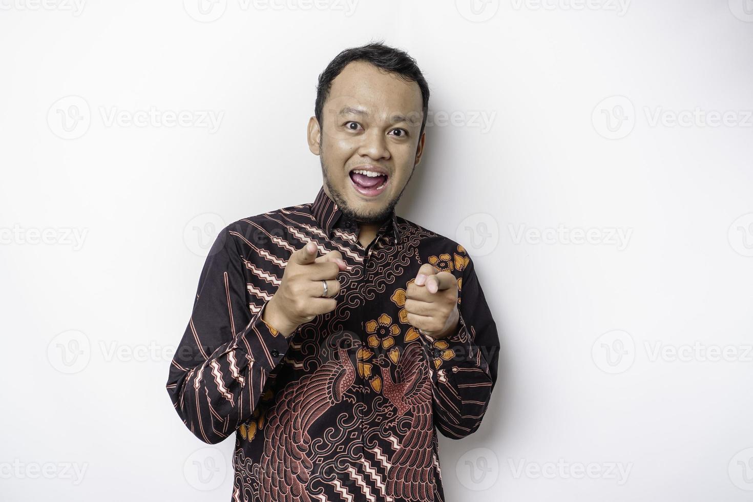 giovane asiatico uomo indossare batik camicia in piedi al di sopra di isolato bianca sfondo puntamento dita per telecamera con contento viso. bene energia e vibrazioni. foto