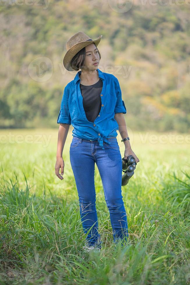 donna indossare cappello e hold binoculare nel erba campo foto