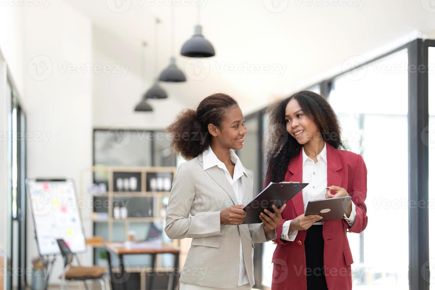 sorridente diverso colleghi donne d'affari Lavorando su il computer portatile insieme, guardare a schermo, In piedi a scrivania nel ufficio, dipendenti discutere progetto strategia, condivisione idee foto