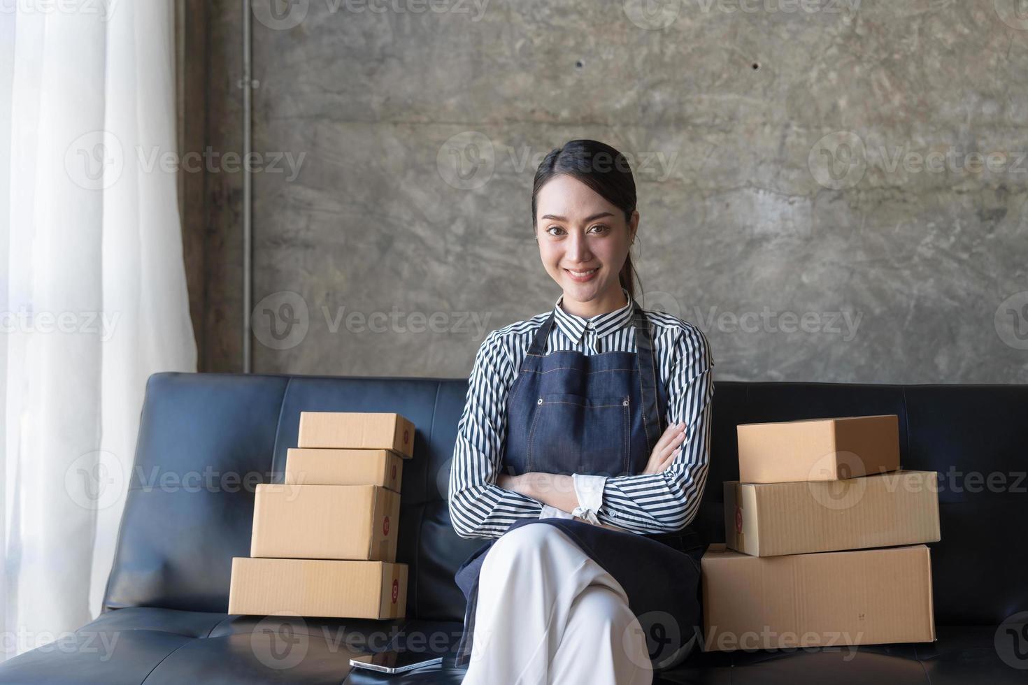 giovane asiatico attività commerciale donna su divano utilizzando il computer portatile computer controllo cliente ordine in linea spedizione scatole a casa. foto