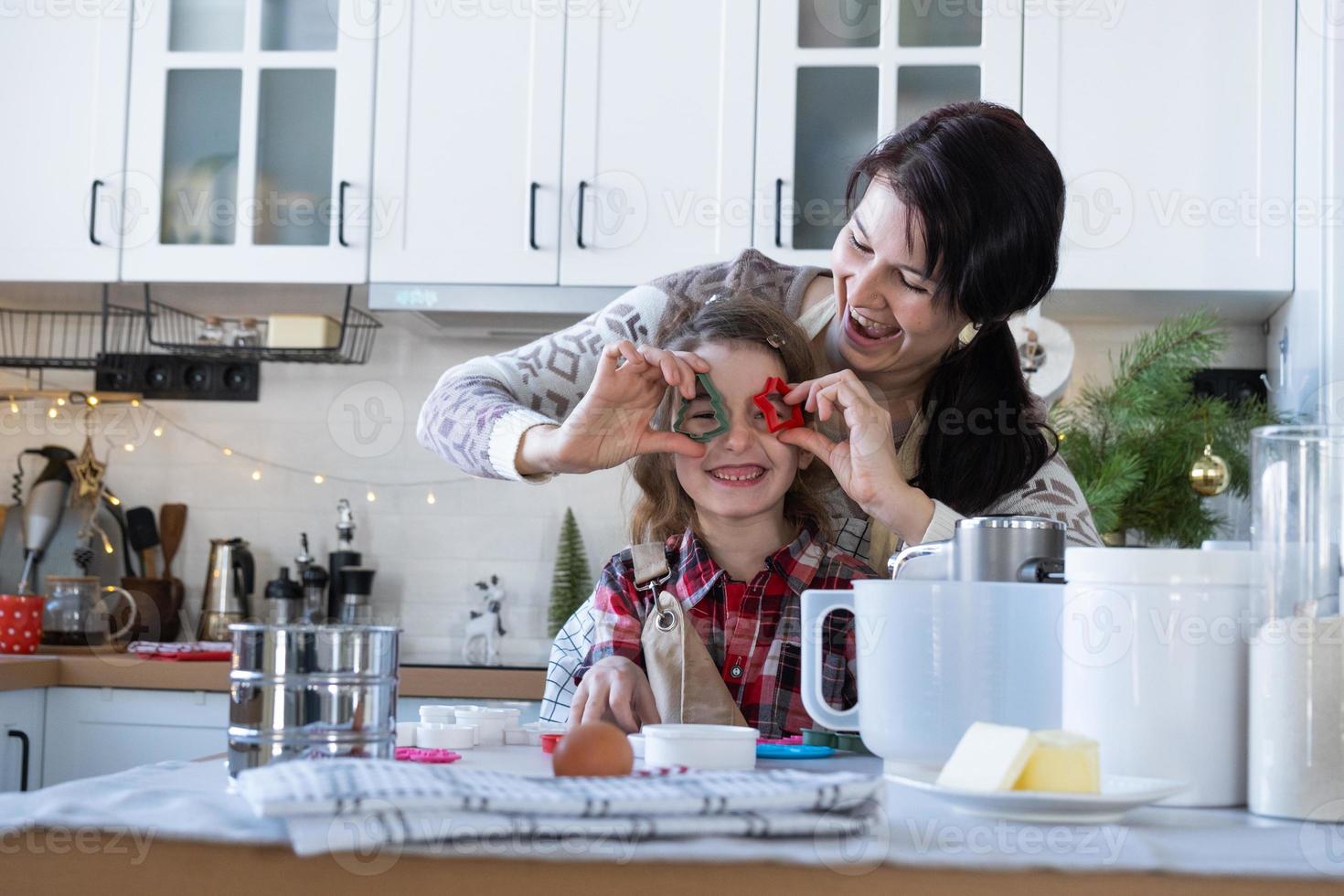 mamma e figlia nel il bianca cucina siamo preparazione biscotti per Natale e nuovo anno. famiglia giorno, preparazione per il vacanza, imparare per cucinare delizioso pasticcini, tagliare forme su di Impasto con muffe foto