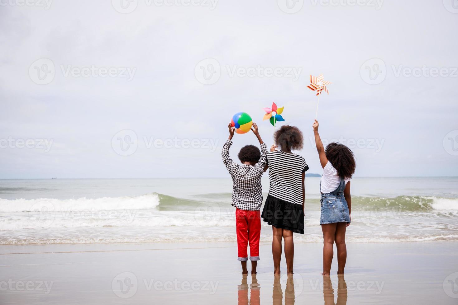 indietro lato di africano americano bambini in piedi su un' tropicale spiaggia. etnicamente diverso concetto foto