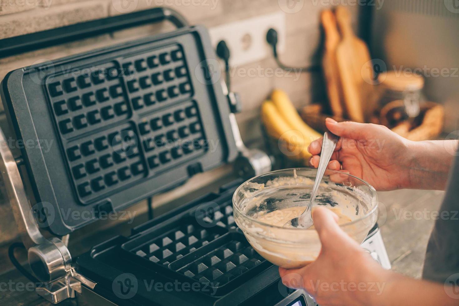 giovane donna preparazione belga cialde nel il cucina. cucinando processi foto