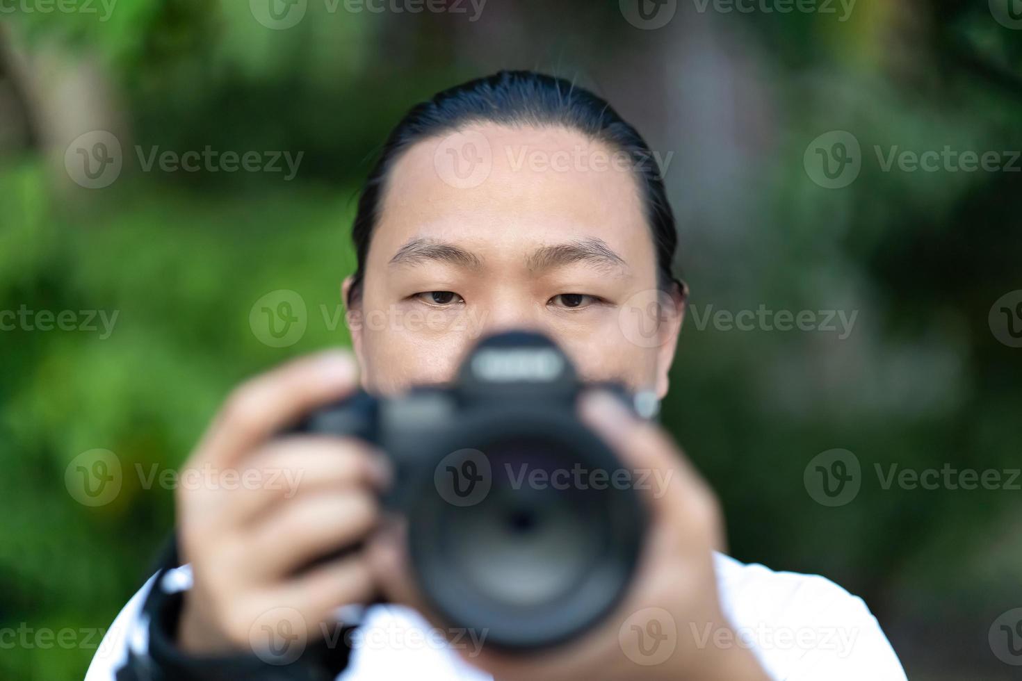 messa a fuoco su il asiatico uomo viso quello lui detiene il sfocatura medio formato telecamera nel il suo mano e preparare per sparare nel davanti di lui. foto