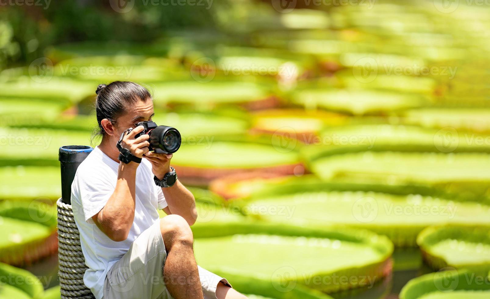 asiatico uomo è Tenere un' telecamera e assunzione un' foto a all'aperto campo con il giglio loto foglia stagno sfondo.