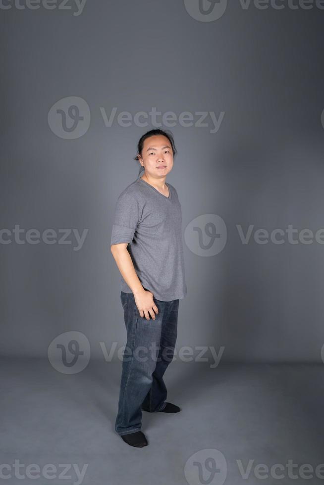 asiatico lungo capelli amichevole e positivo uomo è spedizione e in piedi nel davanti di grigio sfondo con studio luce. foto