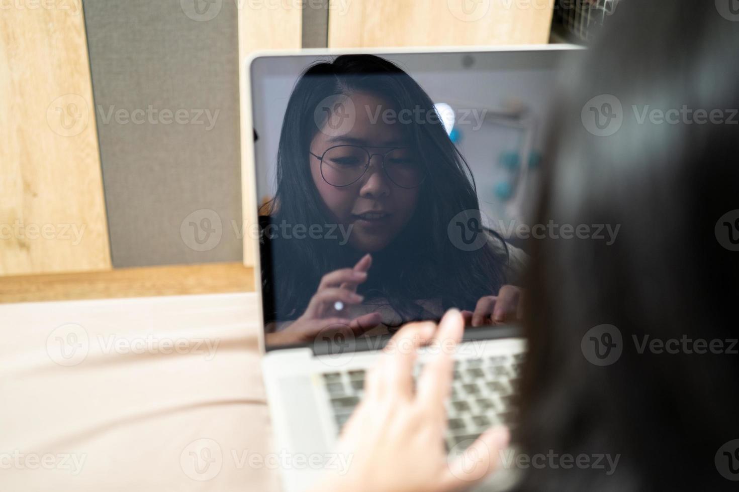 il riflessione di bellissimo asiatico donna a partire dal il computer portatile schermo. lei giochi il computer portatile e stabilisce su il letto nel sua Camera da letto. foto