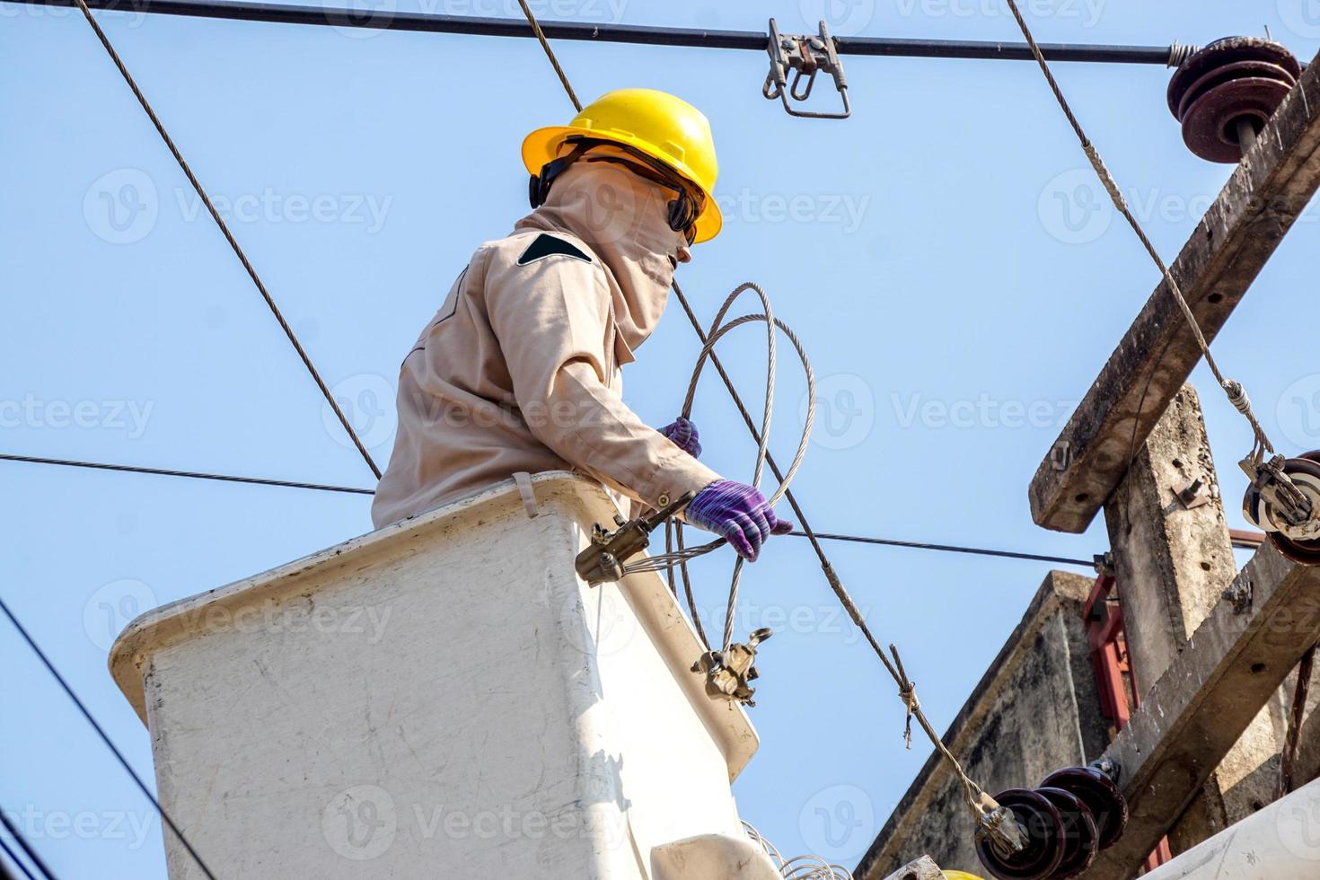 avvicinamento elettricisti Lavorando su cavo auto per riparazione il energia linea sotto leggero blu cielo sfondo. foto