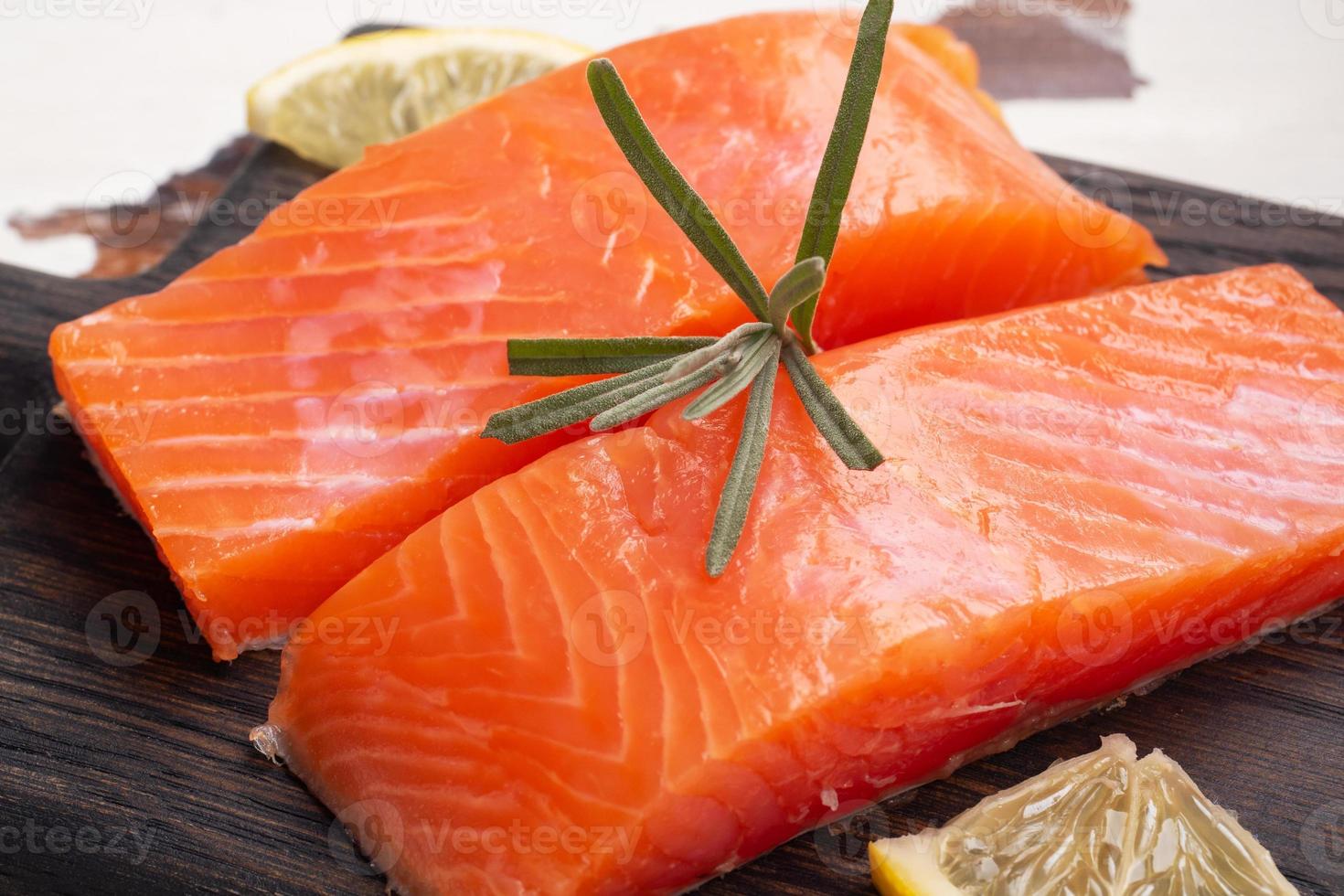 filetto di salmone, pesce rosso salato su un tagliere di legno. limone, spezie al rosmarino. foto