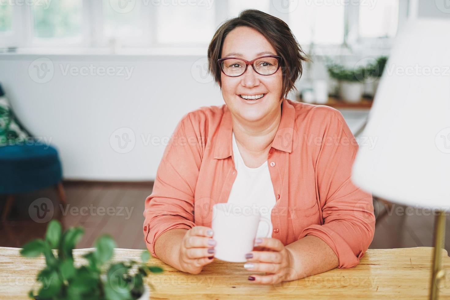 adulto affascinante brunetta donna nel bicchieri più dimensione corpo positivo con tazza di tè a casa foto