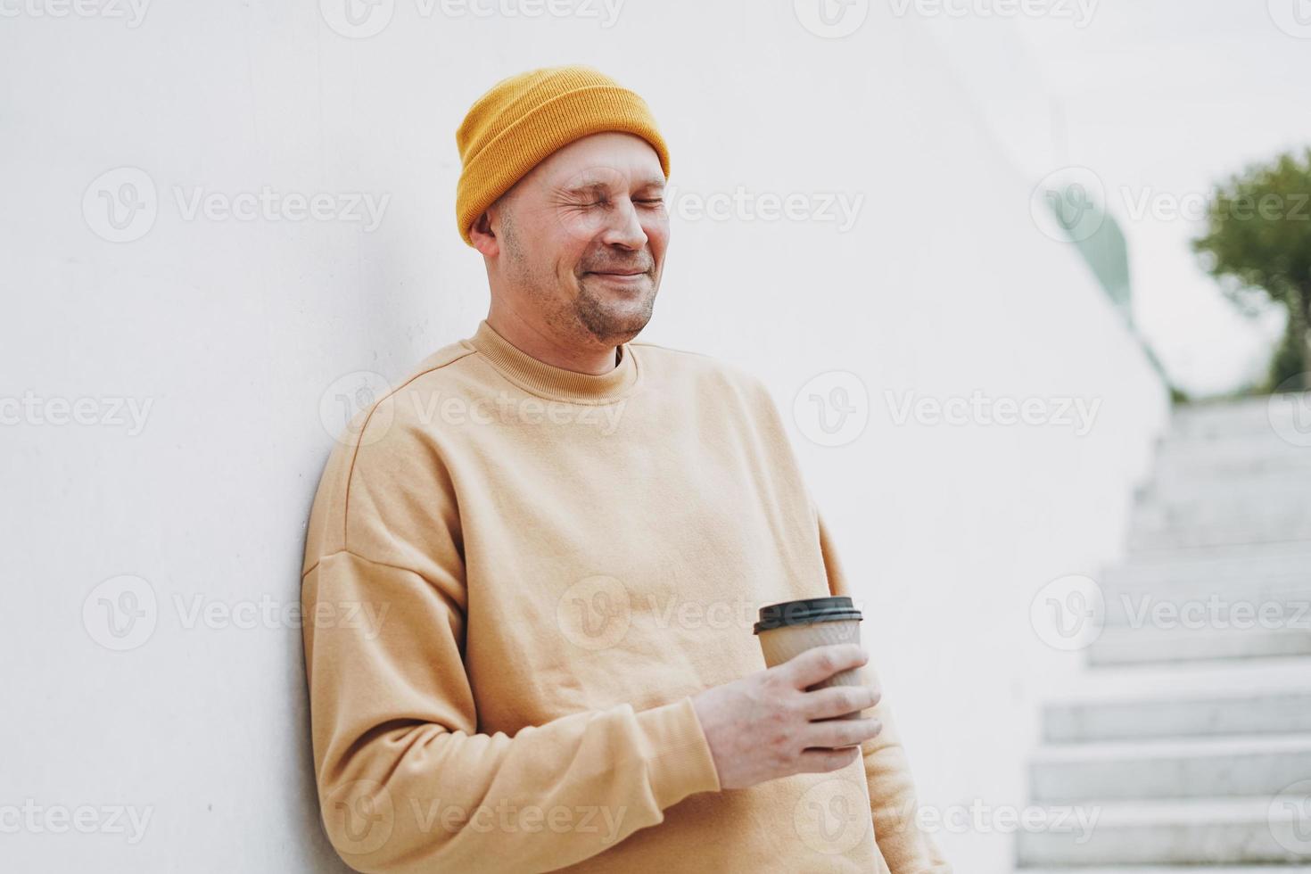 ritratto di elegante uomo fricchettone nel giallo cappello con carta tazza di caffè a il città foto
