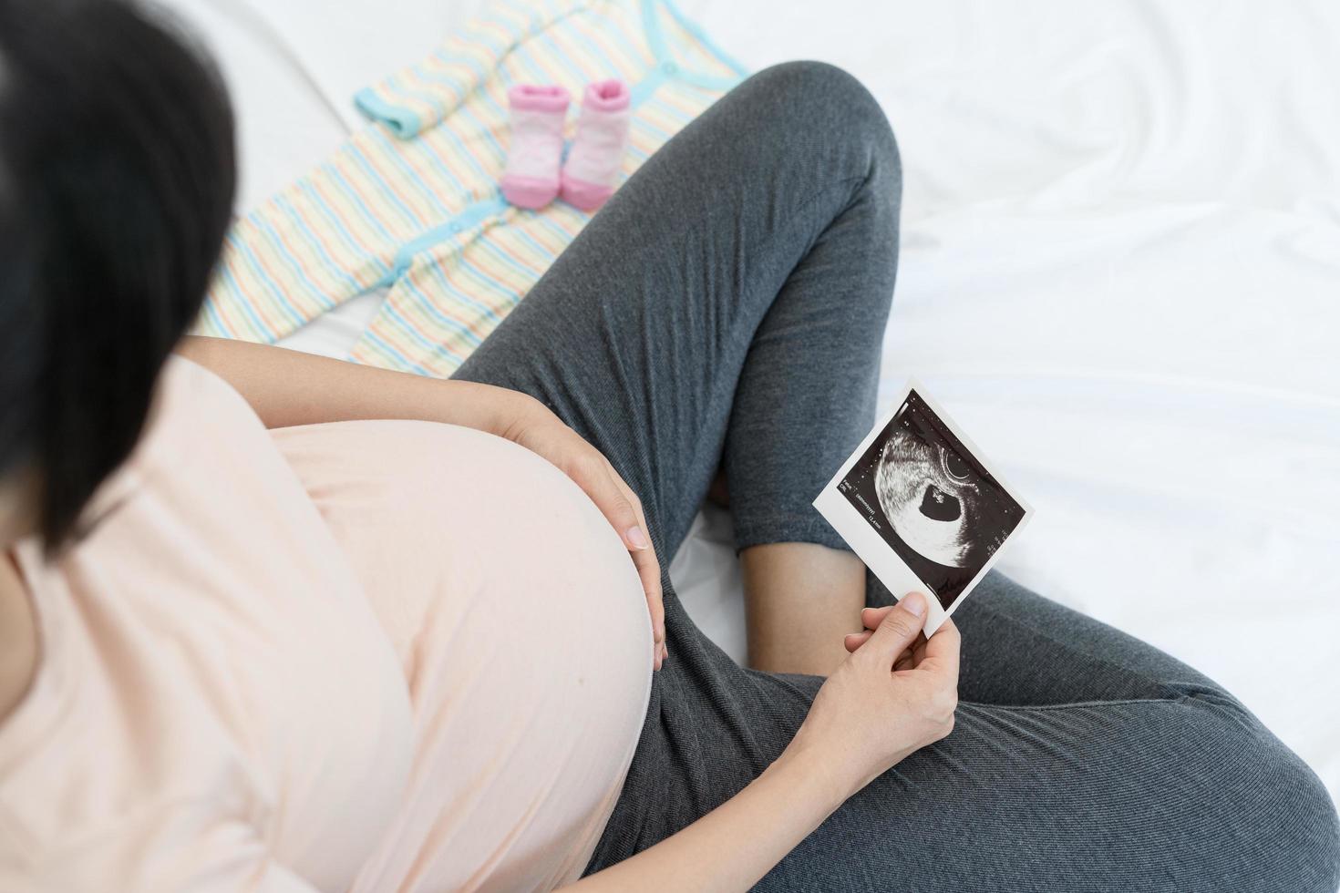 un' incinta donna è guardare a un ultrasuono foto di feto. madre delicatamente tocchi il bambino su stomaco.donne siamo incinta per 2-3 giorni o durante il primo trimestre.