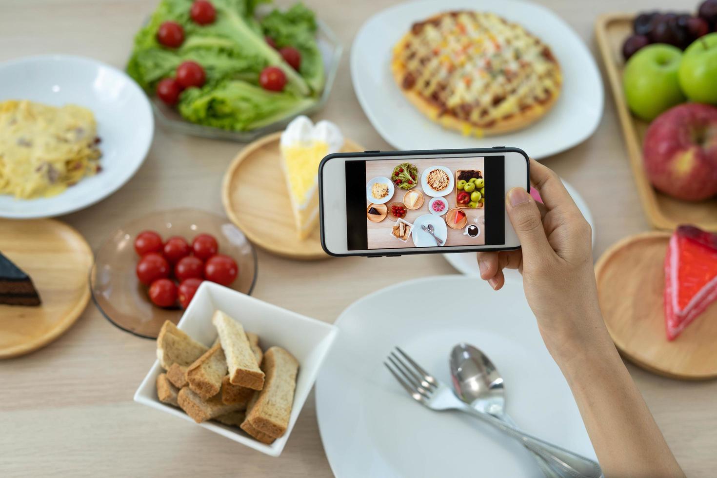 la mano di un recensore che utilizza un telefono cellulare per scattare foto del cibo al tavolo di un ristorante. Scatta una foto per scrivere una recensione del ristorante da condividere su Internet.