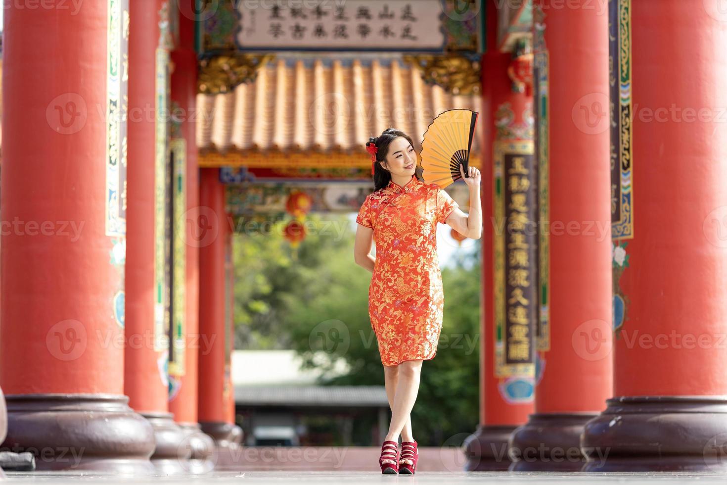 asiatico donna nel rosso cheongsam qipao vestito Tenere carta fan mentre visitare il Cinese buddista tempio durante lunare nuovo anno per tradizionale cultura concetto foto