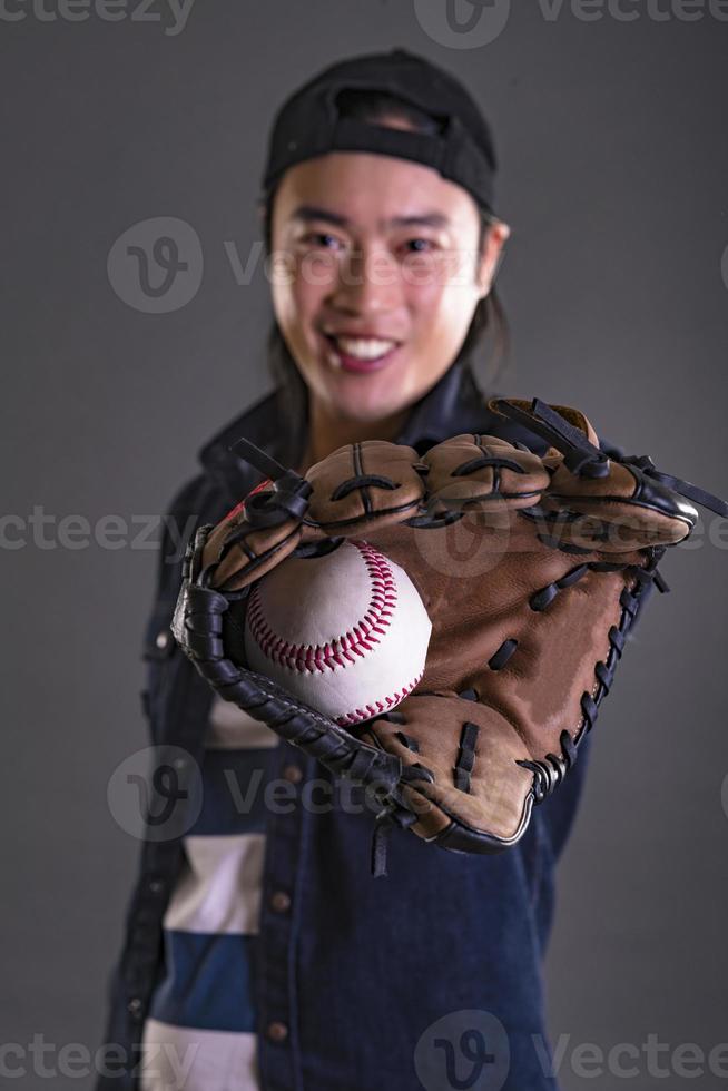 asiatico uomo giocando baseball. Tenere baseball e indossare baseball guanto. isolato su grigio sfondo foto