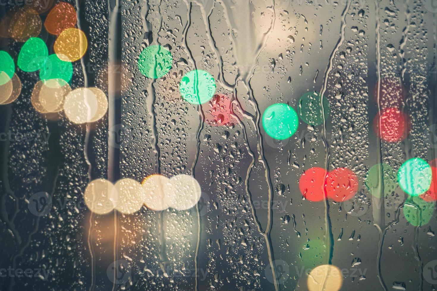 gocce di pioggia su il finestra e strada luci sfondo a notte foto