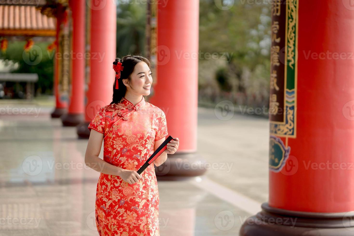 un' asiatico donna indossare tradizionale cheongsam qipao vestito Tenere fan e Sorridi mentre visitare il Cinese buddista tempio. Cinese nuovo anno concetto foto