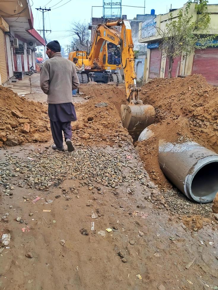 scavatrice scavare il trincee a un' costruzione luogo. trincea per posa esterno fogna tubi. liquame drenaggio sistema nel Pakistan foto