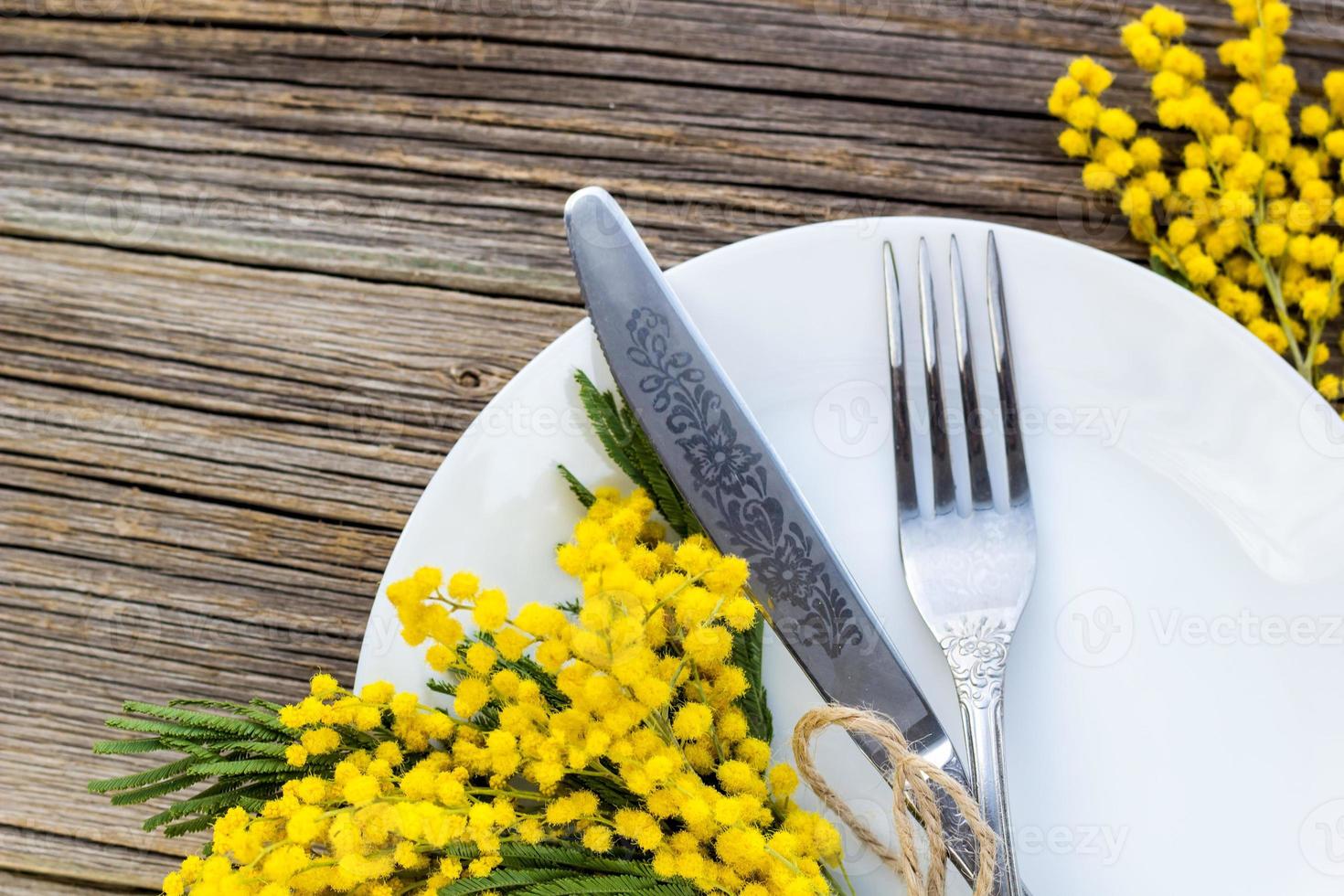 forchetta coltello con piatto e mimosa fiori su di legno tavolo per primavera Pasqua vacanza cena. foto