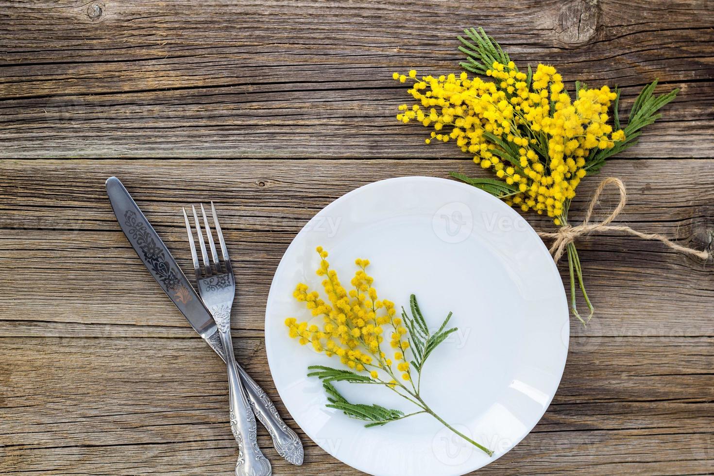 forchetta coltello con piatto e mimosa fiori su di legno tavolo per primavera Pasqua vacanza cena. foto