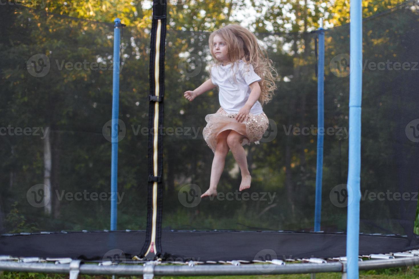 poco bambino ragazza salto su il trampolino nel il indietro cortile foto