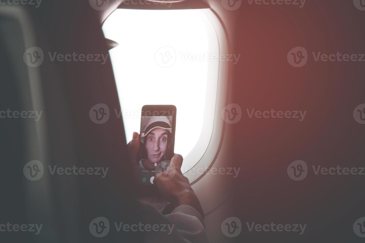 giovane caucasico donna passeggeri posa per autoscatto toccare toccare schermo smartphone nel aereo cabina posto a sedere prima volo. divertente ragazze su vacanza inviare su sociale media concetto foto