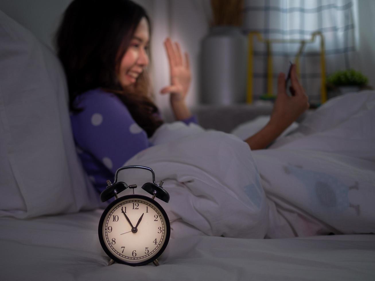 un asiatico donna è utilizzando un' smartphone per rendere video chiamate con sua fidanzato nel letto prima andando per letto a notte. smartphone dipendenza foto